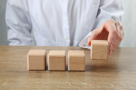 Doctor with blank cubes at wooden table, closeup. Mockup for designの写真素材