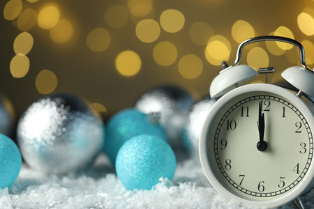 Alarm clock and shiny baubles on artificial snow against golden background with blurred lights,...