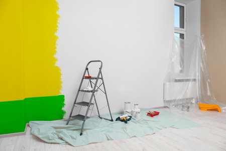 Choosing color for interior. Decorator's tools and paint on floor in room near wall partly painted in different shadesの写真素材