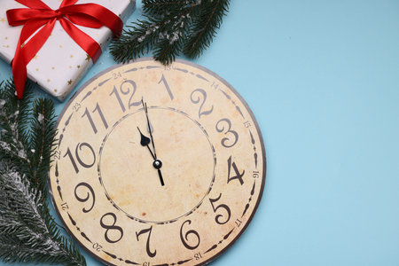Wall clock, fir tree branches and gift box on light blue background, flat lay with space for text....