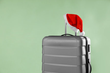 Gray suitcase with Santa hat on olive background, closeup. Space for textの写真素材