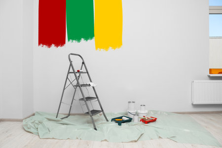 Choosing color for interior. Decorator's tools and paint on floor in room near wall partly painted in different shadesの写真素材