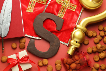 Saint Nicholas (Sinterklaas) day. Stole, crosier, book, feather, chocolate letter S, kruidnoten cookies and gift box on red background, flat layの写真素材