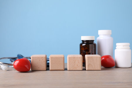 Stethoscope, pills, heart figures and blank cubes on wooden table against light blue background. Mockup for designの写真素材