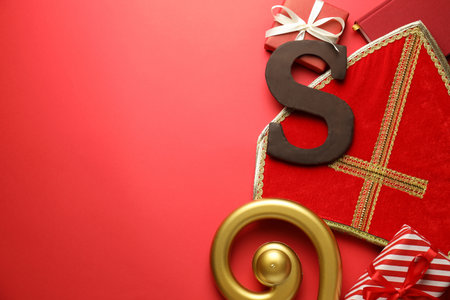 Saint Nicholas (Sinterklaas) day. Miter, crosier, chocolate letter S and gift boxes on red background, flat lay. Space for textの写真素材