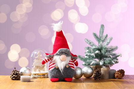 Christmas gnome and festive decor on wooden table against color background with blurred lights. Bokeh effectの写真素材