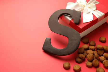 Saint Nicholas (Sinterklaas) day. Chocolate letter S, kruidnoten cookies and gift box on red background, closeup. Space for textの写真素材