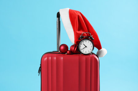 Christmas vacation. Red suitcase with Santa hat, baubles and alarm clock on light blue backgroundの写真素材
