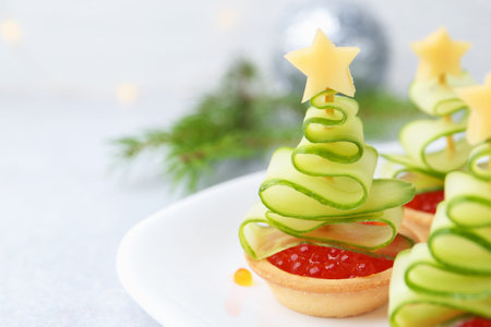 Christmas tree shaped tartlets made with red caviar, cucumber, cheese and festive decor on white table, closeupの写真素材
