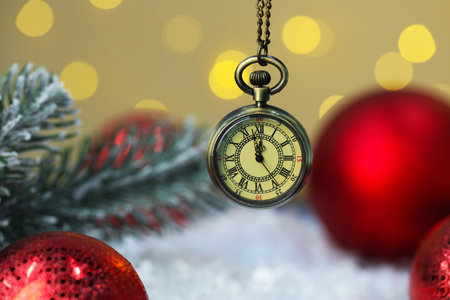 Pocket watch, shiny baubles, fir branches and artificial snow against blurred lights, closeup. New...