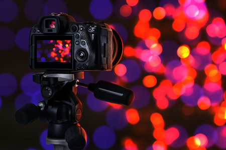 Professional camera against blurred lights on dark background, bokeh effectの写真素材