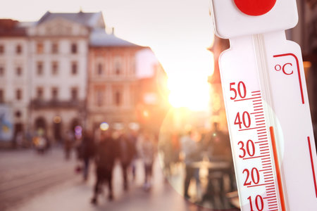 Thermometer showing high temperature against city during hot dayの写真素材