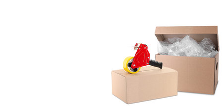 Cardboard boxes, bubble wrap and dispenser with adhesive tape on white background