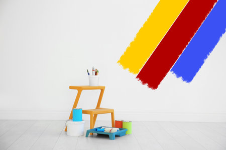 Choosing color for interior. Decorator's tools and paint on floor in room near wall partly painted in different shadesの写真素材