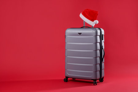 Christmas vacation. Gray suitcase with Santa hat on red background, space for textの写真素材