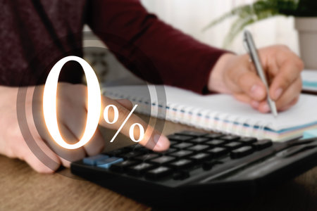 Man using calculator and taking notes at table, closeup. 0 percent representing zero commissionの写真素材