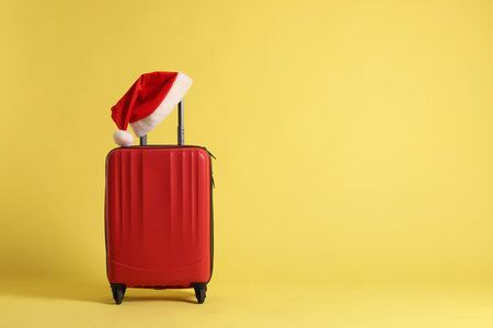 Stylish suitcase with Santa hat on yellow background, space for text. Christmas vacationの写真素材