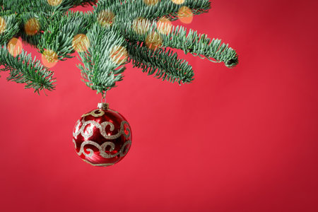 Beautiful Christmas ball hanging on fir tree branch against red backgroundの写真素材