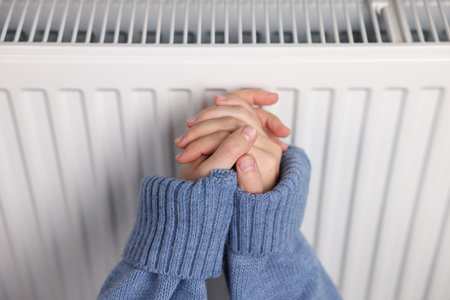 Woman warming her hands near radiator indoors, closeupの写真素材