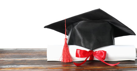 Diploma and graduation hat on wooden table against white backgroundの写真素材