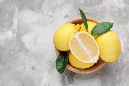Whole and cut lemons with green leaves in bowl on gray textured table, top view. Space for textの写真素材