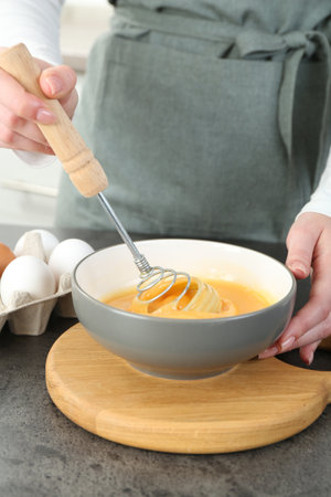 Woman beating eggs at gray table in kitchen, closeup