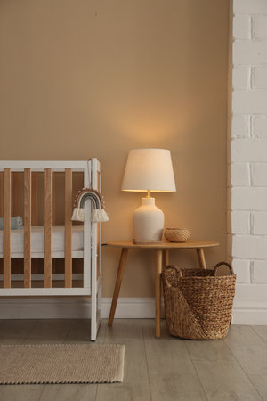 Crib, table, lamp and decor near beige wall indoors. Stylish baby's room interiorの写真素材