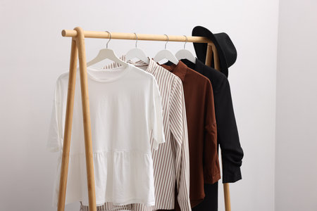 Different stylish clothes hanging on rack near light wall indoorsの写真素材