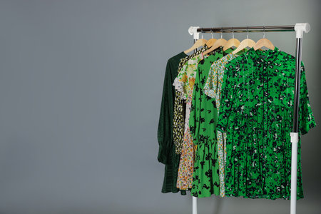 Different stylish clothes hanging on rack against gray background, space for textの写真素材