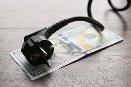 Electrical wire with plug and dollar banknote on wooden table, closeupの写真素材