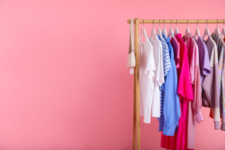 Different clothes and bag hanging on rack against pink background, closeup. Space for textの写真素材
