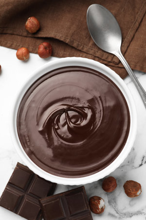 Melted chocolate in bowl, pieces, nuts and spoon on white marble table, flat layの写真素材