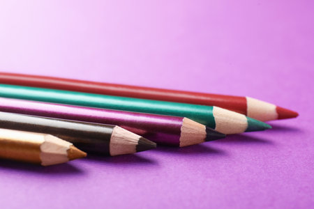 Different eye pencils on purple background, closeup