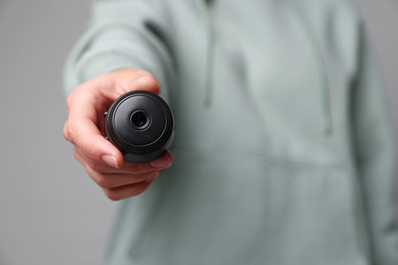 Young woman with hidden spy camera on light gray background, closeup