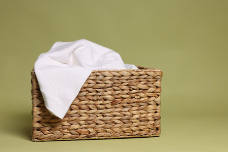 Wicker basket full of laundry against olive backgroundの写真素材