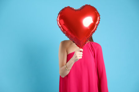 Woman hiding behind heart shaped balloon on light blue background. Romantic giftの写真素材