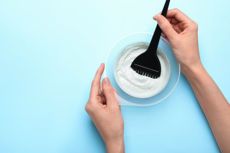 Woman preparing hair dye in bowl on light blue background, top view. Space for textの写真素材