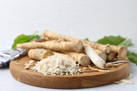 Whole and gratified horseradish roots, peeler and green leaves on light gray table, closeupの写真素材