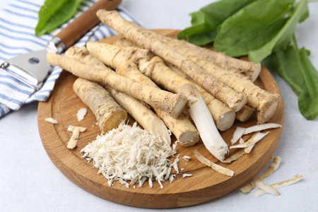 Whole and gratified horseradish roots, peeler and green leaves on light gray table, closeupの写真素材