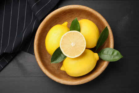 Fresh lemons with green leaves on black wooden table, top viewの写真素材