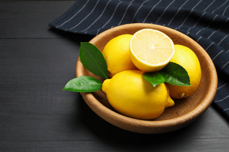 Fresh lemons with green leaves on black wooden table, closeup. Space for textの写真素材