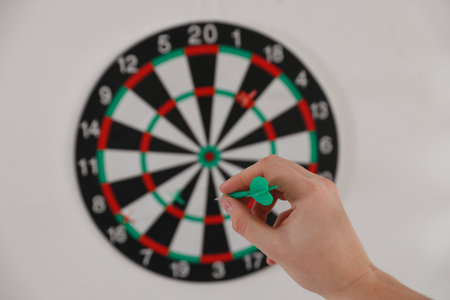Man with dart aiming at dartboard indoors, selective focus