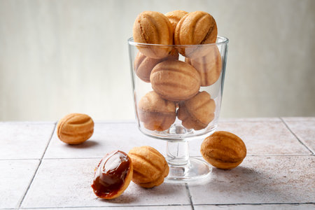 Delicious nut shaped cookies with boiled condensed milk on light tiled table, closeup