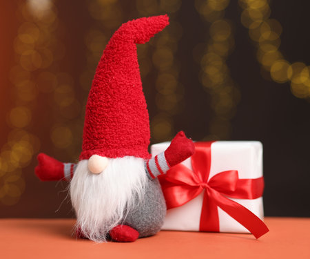 Christmas gnome and gift box on color table against dark orange background with blurred lights. Bokeh effectの写真素材