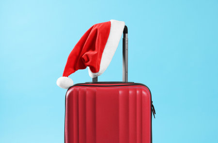 Christmas vacation. Red suitcase with Santa hat on light blue backgroundの写真素材