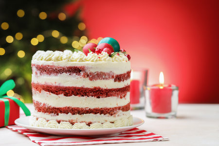 Delicious sponge cake with Christmas decor on white table against red background with blurred lights, closeup with space for text. Bokeh effectの写真素材