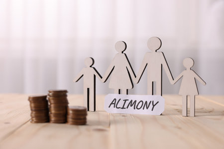 Paper note with word Alimony, figures of family and stacked coins on wooden table, closeupの写真素材