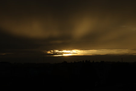 Setting sun shining through clouds over city in evening