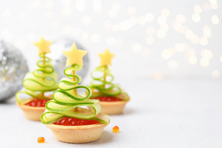 Christmas tree shaped tartlets made with red caviar, cucumber, cheese and festive decor on white table, closeupの写真素材