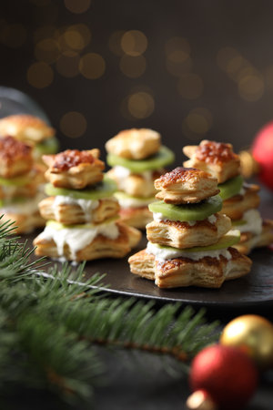 Sweet snacks made of puff pastry, slices of kiwi and Christmas decor on dark table against blurred lights, closeupの写真素材